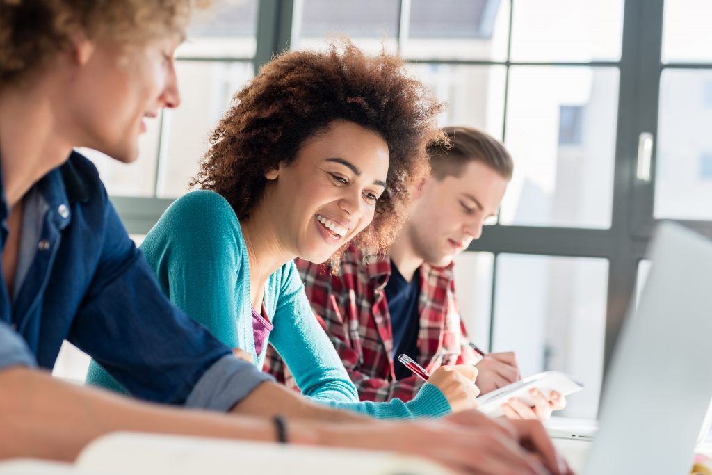 Cheerful Woman Writing An Assignment While Sitting Between Two Classmates