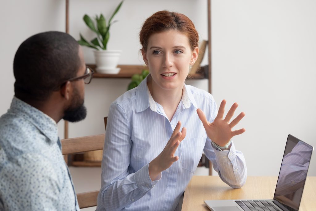 Two Diverse Businesspeople Chatting Sitting Behind Laptop In Office