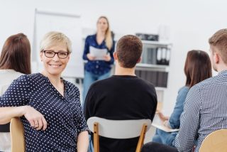 A happy woman wearing glasses smiling at the camera during an office meeting with other colleagues.