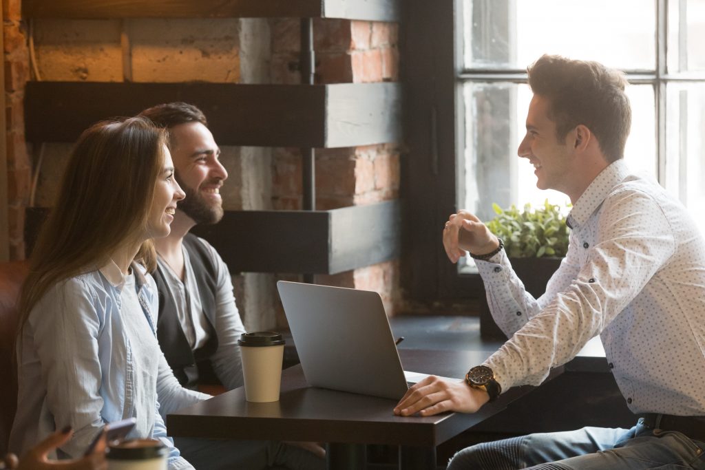 Male Architect Consulting Excited Millennial Couple In Coffee Sh