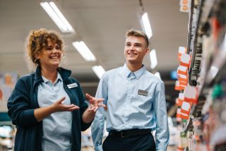 Local grocery store manager training new male employee. Woman explaining inventory system supermarket to young worker.